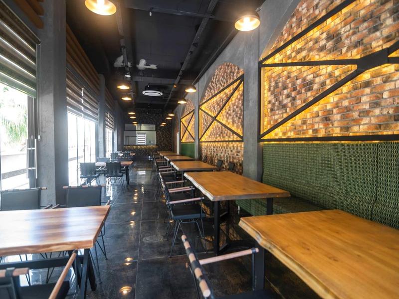 Restaurante moderno del hotel con mesas de madera, bancos verdes y pared iluminada cálidamente.