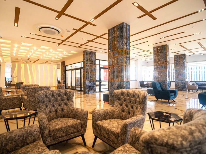 Amplia zona de lounge en hotel con sillones cómodos, grandes ventanas e iluminación brillante.