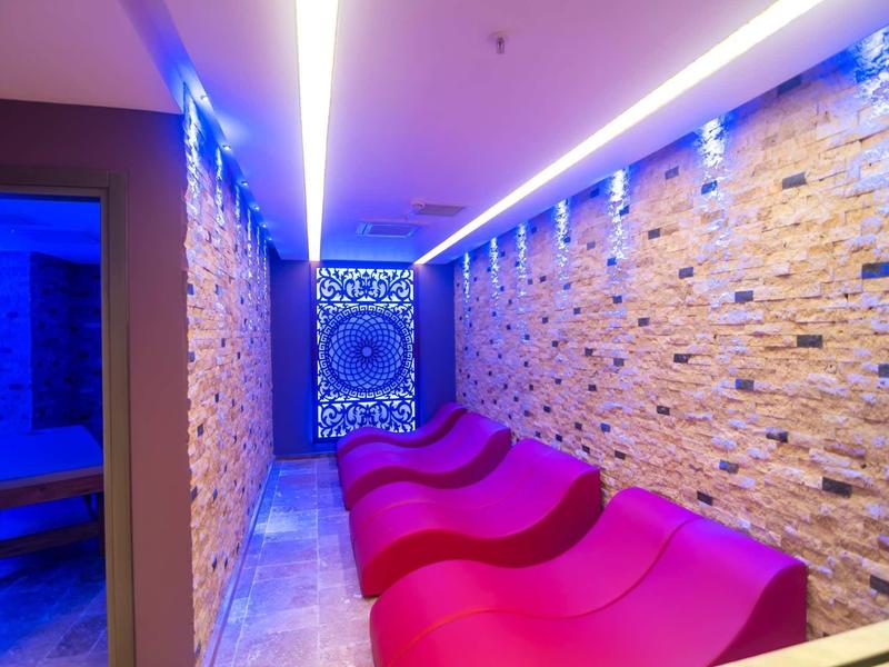 Pasillo iluminado con luces LED azules, paredes de piedra y sillones morados curvos para descanso.