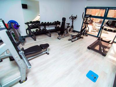 Helles Fitnessstudio mit Laufband, Hanteln, Trainingsgeräten und hellem Holzboden.