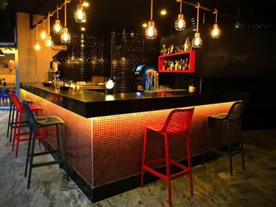 Moderne Bar mit schwarzer Theke, roten und schwarzen Stühlen, warmen Lichtern und Betonboden.