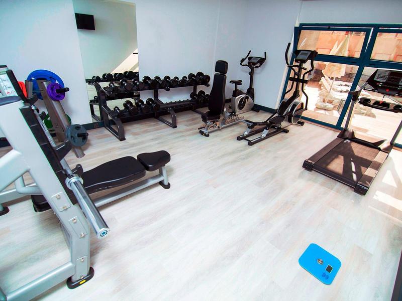 Moderne fitnessruimte met diverse trainingsapparaten en halters bij grote ramen.