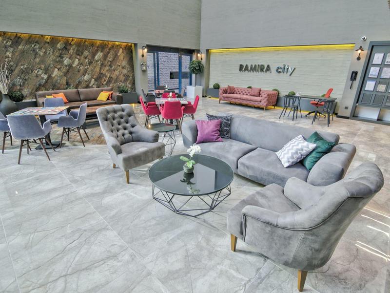 Moderne hotel lounge met comfortabele grijze fauteuils, banken en glazen tafel op lichtgrijze vloer.