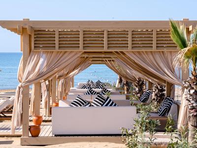 Padiglione sulla spiaggia con tende bianche, divani e cuscini a righe con vista sul mare.