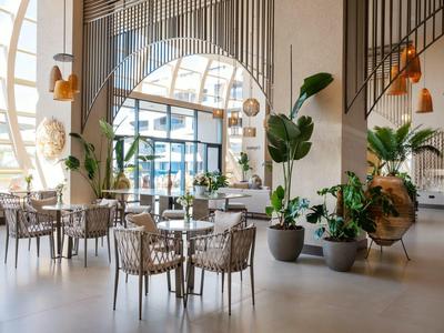 Ristorante d'hotel luminoso e moderno con piante, grandi finestre e tavoli rotondi con sedie.