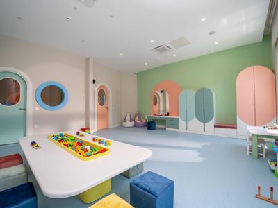 Stanza giochi per bambini luminosa e colorata con tavolo da gioco, sgabelli e decorazioni murali fantasiose.