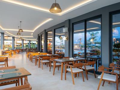 Ristorante d'hotel moderno con tavoli in legno e grandi finestre in vetro, illuminazione luminosa.