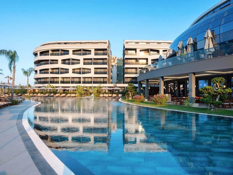 Complesso alberghiero moderno con grande piscina all'aperto e facciata in vetro sotto cielo sereno.