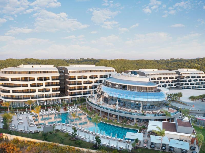 Hotel moderno con edifici curvi e più piscine in un paesaggio verde.