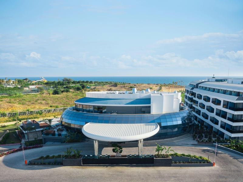 Complesso alberghiero moderno con ingresso circolare e vista sul mare sullo sfondo.