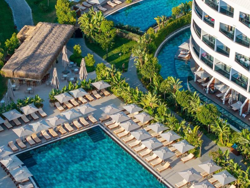 Piscina moderna dell'hotel con lettini e giardino verde accanto a un edificio circolare.