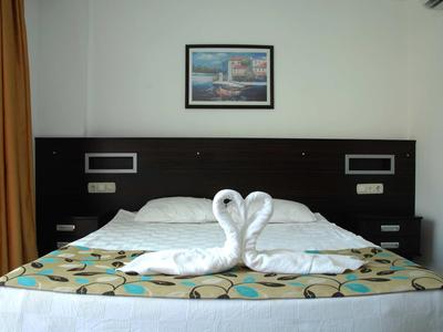 Hotelový pokoj s manželskou postelí, dvěma ručníky ve tvaru labutí a obrazem nad čelem postele.