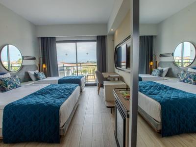 Modern hotel room with two beds, blue bed covers, and balcony overlooking the sea.