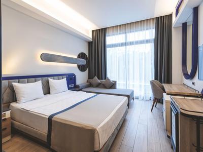 Nowoczesny pokój hotelowy z podwójnym łóżkiem, biurkiem i dużym oknem z zasłonami.