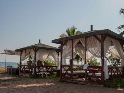 Dwa drewniane pawilony na plaży z białymi zasłonami i morzem w tle.