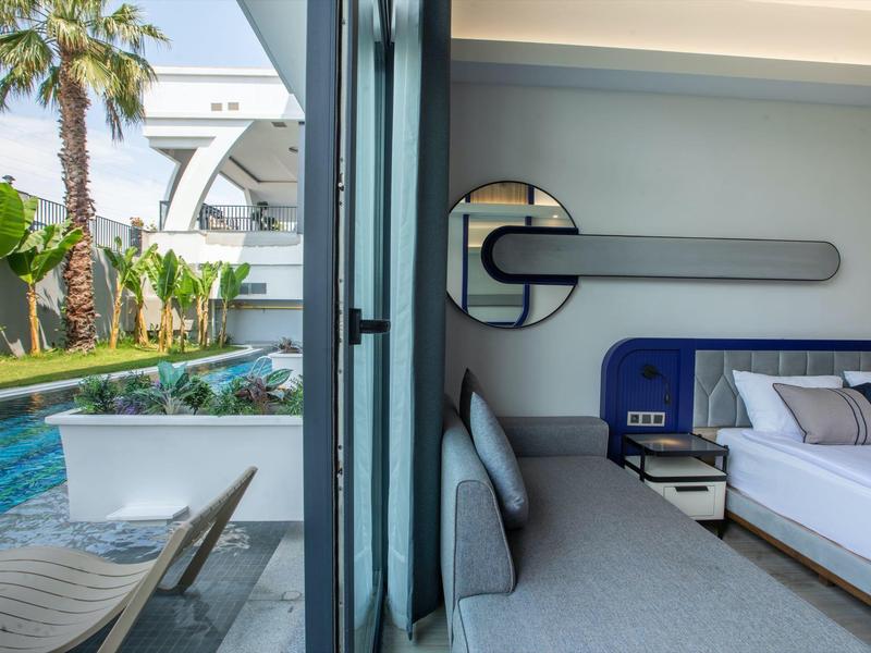 Modern hotel room with sofa, bed, and view of pool and palm trees.