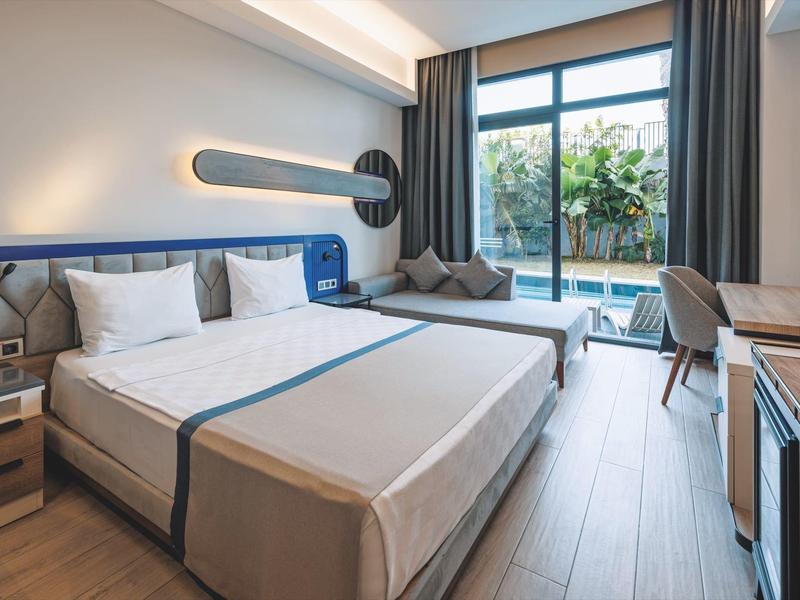 Modern hotel room with double bed, large window, and terrace seating area.