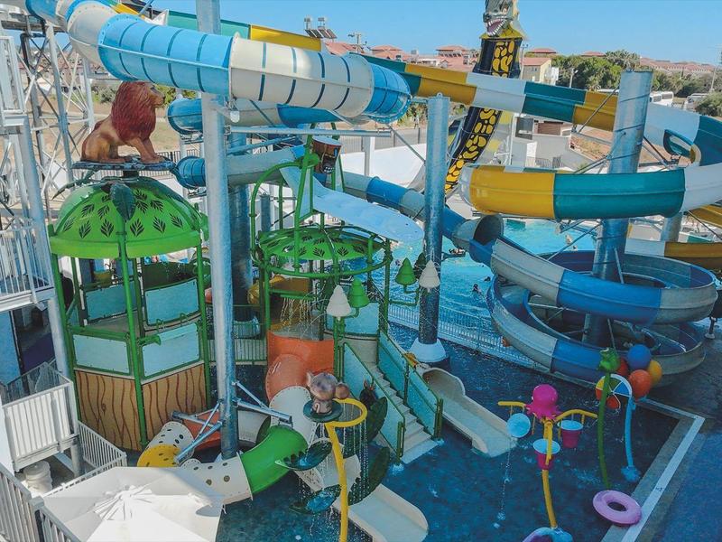 Colorful water park with water slides and play areas, surrounded by lounge chairs and sea view.