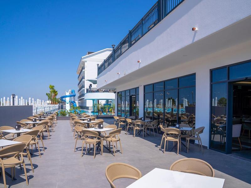 Sunny terrace with tables and chairs in front of modern hotel building.