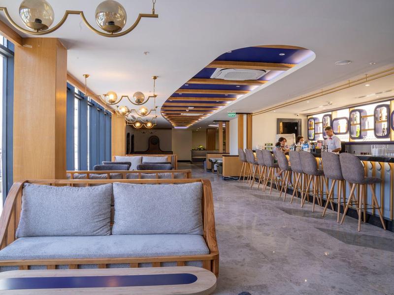 Modern hotel lounge with seating, bar, and large windows showcasing city views.