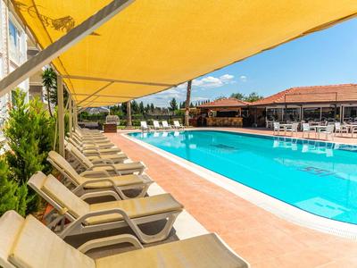 Rij ligstoelen onder gele luifel naast groot buitenzwembad bij hotel.