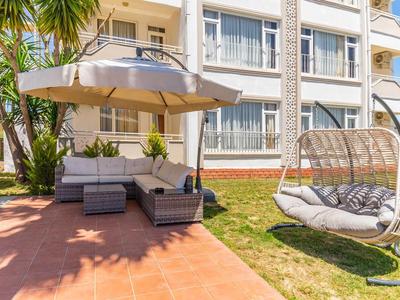 Zithoek met loungeset en schaduwrijke parasol naast een hangende rotan stoel in de tuin.