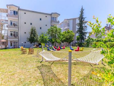 Area esterna soleggiata con amache, sedute e spazi verdi davanti a un edificio residenziale.