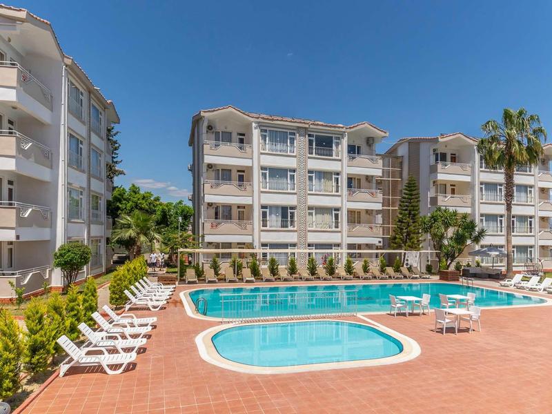 Modern vakantiecomplex met meerdere gebouwen en twee zwembaden onder een heldere hemel.