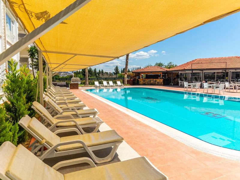 Rij ligstoelen onder gele luifel naast groot buitenzwembad bij hotel.