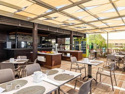 Jasná venkovní terasa s stolky a židlemi pod skleněnou střechou v hotelové restauraci.