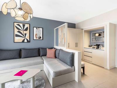 Moderní obývací pokoj s velkou rohovou pohovkou, dvěma obrazy na zdi a otevřenou kuchyní.