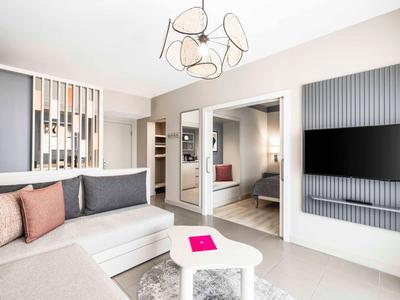 Moderně zařízený hotelový pokoj s pohovkou, konferenčním stolkem a televizí na zdi.