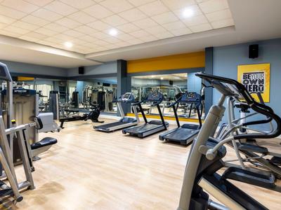 Lichte fitnessruimte met loopbanden, crosstrainers en spiegels aan de muren.