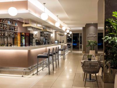 Moderní hotelový bar s osvětleným pultem, vysokými stoličkami a útulnými sezeními.