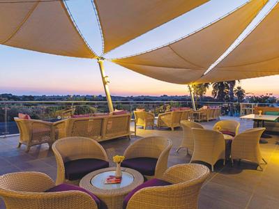 Terras met rotan stoelen en zonneschermen met uitzicht op een landschap bij zonsondergang.