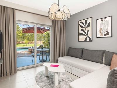 Obývací pokoj se šedou rohovou sedačkou, malým bílým stolem a přístupem na terasu s bazénem