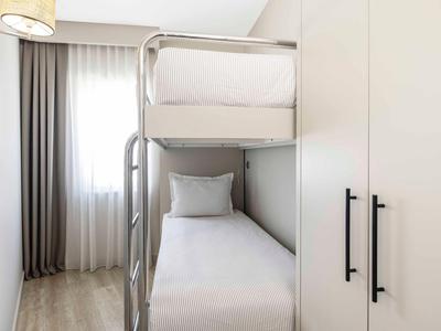 Malá ložnice s palandou vedle bílé skříně a závěsů u okna.