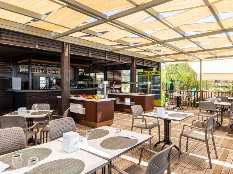 Jasná venkovní terasa s stolky a židlemi pod skleněnou střechou v hotelové restauraci.