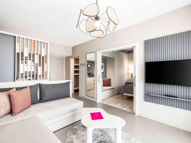 Moderně zařízený hotelový pokoj s pohovkou, konferenčním stolkem a televizí na zdi.