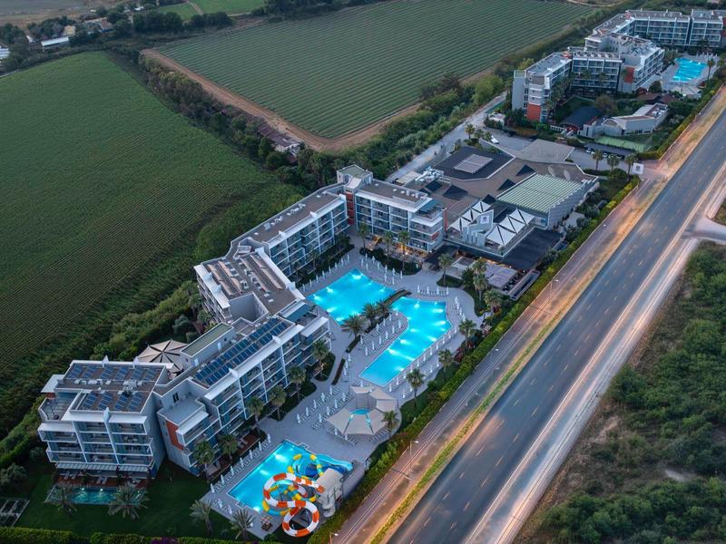 Letecký pohled na hotel s velkými bazény vedle dálnice a polí.