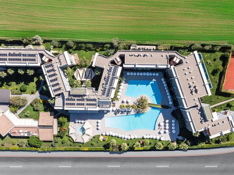 Letecký pohled na resort s velkým bazénem, tenisovými kurty a okolními poli.