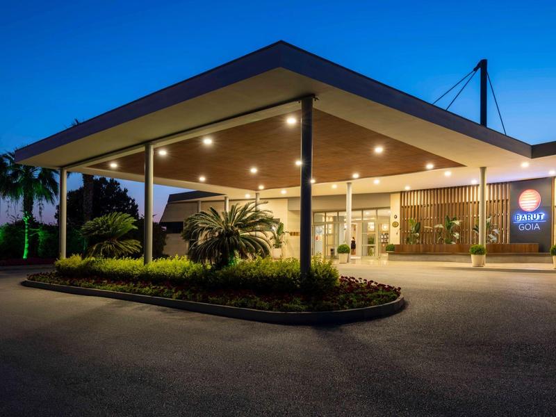 Moderní vchod do hotelu v noci s osvětlenou stříškou a palmami.