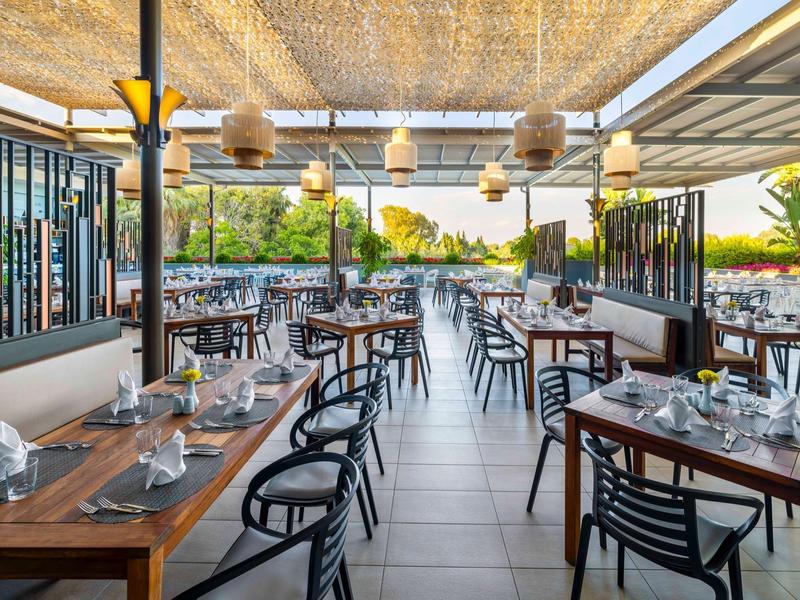 Otevřená restaurace s dřevěným nábytkem a výhledem na vodu při západu slunce.