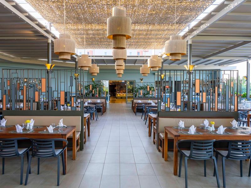 Prostorná otevřená restaurace s moderními stoly a židlemi, osvětlená velkými stropními lampami.