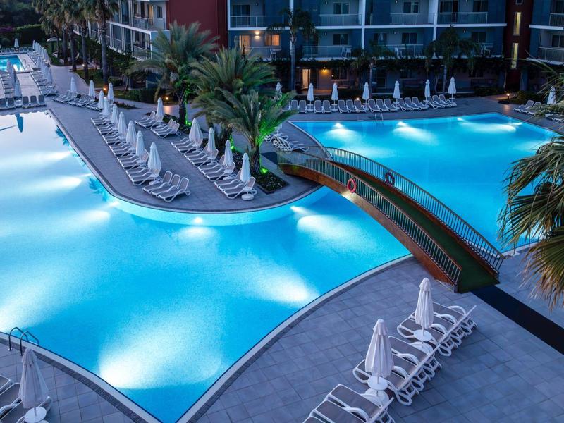 Velká osvětlená bazénová plocha s lehátky a mostky v noci v hotelu.