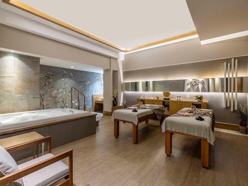 Moderní spa místnost se dvěma masážními stoly, velkou vanou a relaxační atmosférou.