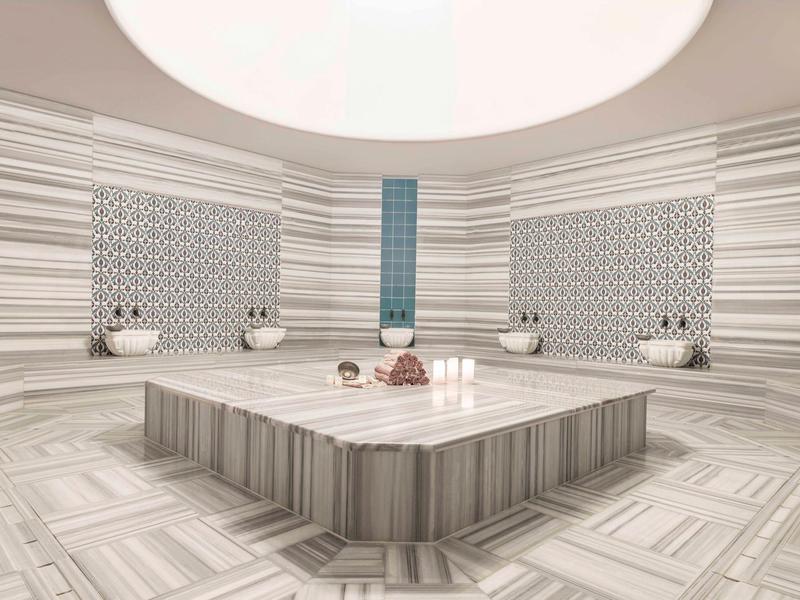 Moderní hammam s centrálním sezením a světlými mramorovými dlaždicemi.