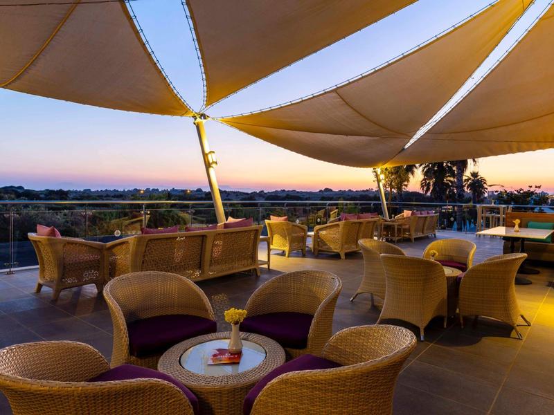 Střešní terasa s ratanovými židlemi a stoly, výhled na krajinu při západu slunce.