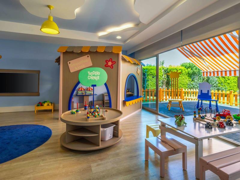 Dětský koutek s dřevěným domečkem, hračkami a stolem v jasném vnitřním prostoru s výhledem na terasu