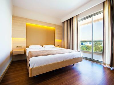 Modern hotel room with double bed, wooden floor and balcony view.